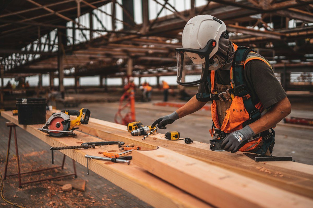 Handwerker mit Schutzhelm und Akkuschrauber bei der Arbeit an einem Holzbalken