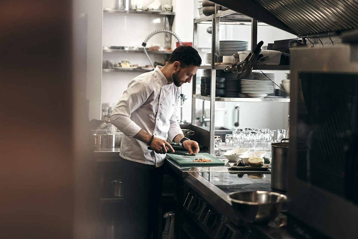Koch in weißer Jacke schneidet Gemüse in einer Restaurantküche